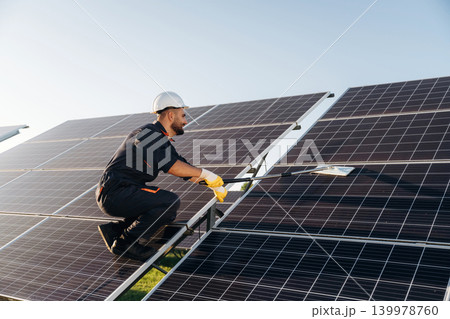 High up, cleaning the surface with a mop. Male solar engineer examining photovoltaic panels at a power station High up, cleaning the surface with a mop. Male solar engineer examining photovoltaic panels at a power station 139978760
