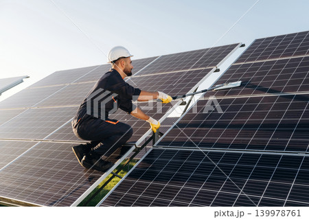 High up, cleaning the surface with a mop. Male solar engineer examining photovoltaic panels at a power station 139978761