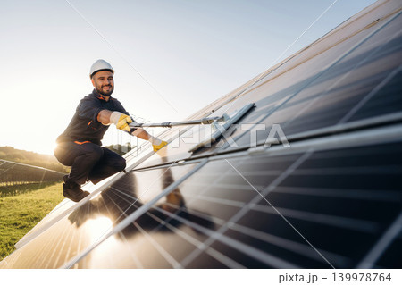 Mopping the surface. Male solar engineer examining photovoltaic panels at a power station Mopping the surface. Male solar engineer examining photovoltaic panels at a power station 139978764