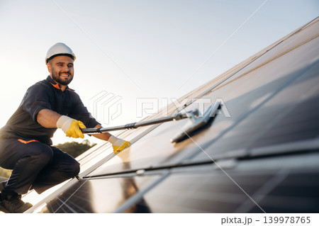 Mopping the surface. Male solar engineer examining photovoltaic panels at a power station Mopping the surface. Male solar engineer examining photovoltaic panels at a power station 139978765
