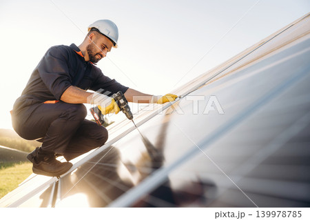 Installation, using the drill. Male solar engineer examining photovoltaic panels at a power station 139978785