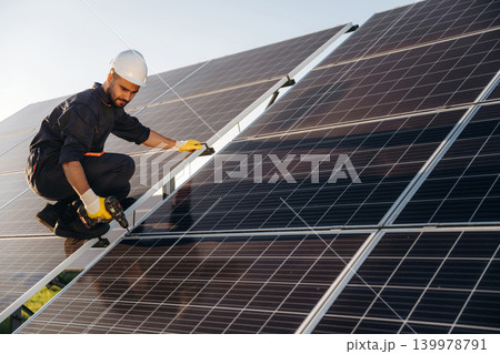 Service, sitting with drill and doing installation. Male solar engineer examining photovoltaic panels at a power station 139978791