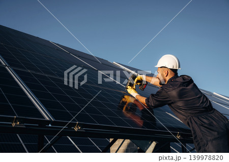 Against clear blue sky, installation process. Male solar engineer examining photovoltaic panels at a power station Against clear blue sky, installation process. Male solar engineer examining photovoltaic panels at a power station 139978820