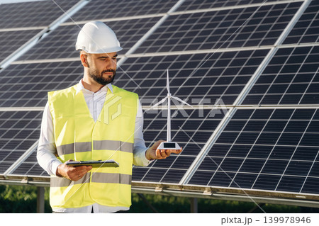Small windmill model. Male solar engineer examining photovoltaic panels at a power station Small windmill model. Male solar engineer examining photovoltaic panels at a power station 139978946