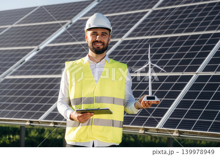 Small windmill model. Male solar engineer examining photovoltaic panels at a power station Small windmill model. Male solar engineer examining photovoltaic panels at a power station 139978949