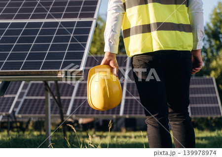 In yellow colored professional uniform. Male solar engineer examining photovoltaic panels at a power station In yellow colored professional uniform. Male solar engineer examining photovoltaic panels at a power station 139978974