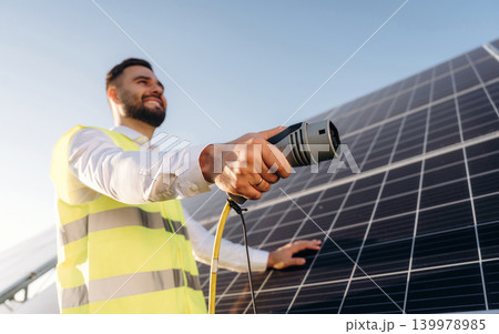 Cable is hand, charging conception. Male solar engineer examining photovoltaic panels at a power station 139978985