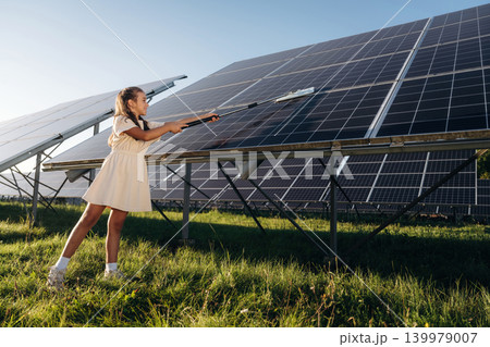 Washing, cleaning the surface. Happy girl is near renewable energy equipment under bright sunlight Washing, cleaning the surface. Happy girl is near renewable energy equipment under bright sunlight 139979007