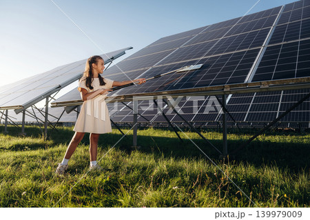 Washing, cleaning the surface. Happy girl is near renewable energy equipment under bright sunlight Washing, cleaning the surface. Happy girl is near renewable energy equipment under bright sunlight 139979009