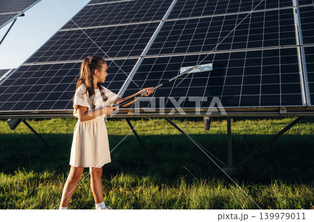 Washing, cleaning the surface. Happy girl is near renewable energy equipment under bright sunlight Washing, cleaning the surface. Happy girl is near renewable energy equipment under bright sunlight 139979011