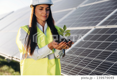 With fresh plant in hands. Female solar engineer inspecting photovoltaic panels during outdoor maintenance work With fresh plant in hands. Female solar engineer inspecting photovoltaic panels during outdoor maintenance work 139979049