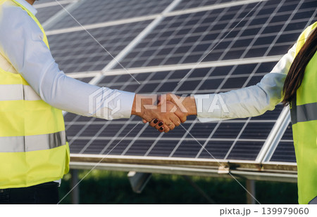 Handshake, cooperation, success. Two solar engineers standing together at a photovoltaic field, in bright safety vests 139979060