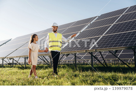 Friendly engineer showing renewable-energy equipment to a young visitor outdoors 139979078