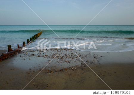 Breakwater, wooden groin, with a calm English Channel coast sea. Watching the water reaching the sand and shingle on a very warm May afternoon 139979103