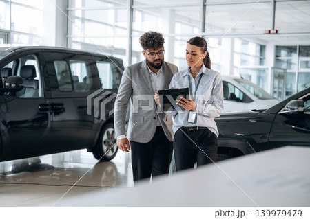 Helping a male customer. Business consultation between car dealer and buyer in showroom Helping a male customer. Business consultation between car dealer and buyer in showroom 139979479
