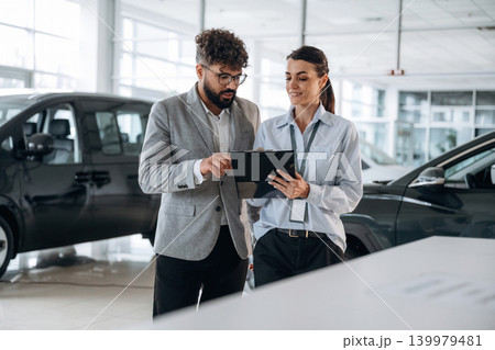 Helping a male customer. Business consultation between car dealer and buyer in showroom Helping a male customer. Business consultation between car dealer and buyer in showroom 139979481