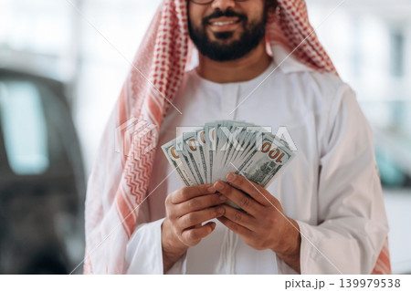 Arab businessman holding cash inside modern car showroom 139979538