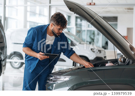 Hood is opened. Auto service specialist examining vehicle condition 139979539