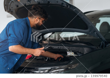 Hood is opened. Auto service specialist examining vehicle condition Hood is opened. Auto service specialist examining vehicle condition 139979540