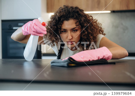 Cleaning the surface. White woman on the the kitchen countertop with spray and cloth wearing pink gloves Cleaning the surface. White woman on the the kitchen countertop with spray and cloth wearing pink gloves 139979684