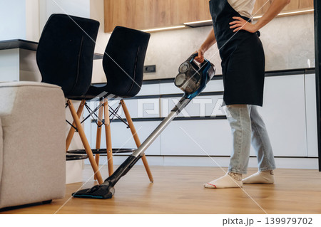 Housewife is vacuuming the floor and cleaning around furniture in a modern kitchen and dining area Housewife is vacuuming the floor and cleaning around furniture in a modern kitchen and dining area 139979702
