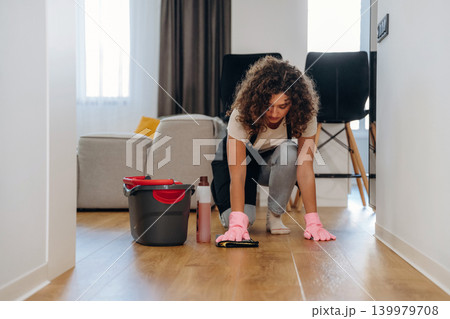 Busy woman cleaning the floor on her knees with a bucket and cloth during household chores Busy woman cleaning the floor on her knees with a bucket and cloth during household chores 139979708