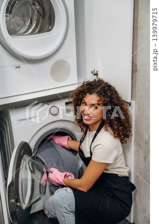 Smiling, cheerful facial expression. At home. Woman doing laundry with washing machine at home Smiling, cheerful facial expression. At home. Woman doing laundry with washing machine at home 139979715