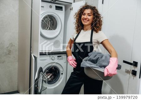 Smiling, cheerful facial expression. At home. Woman doing laundry with washing machine at home Smiling, cheerful facial expression. At home. Woman doing laundry with washing machine at home 139979720