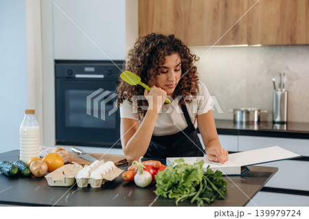 Reading the recipe. Attractive woman preparing fresh vegetables on the kitchen counter during cooking Reading the recipe. Attractive woman preparing fresh vegetables on the kitchen counter during cooking 139979724