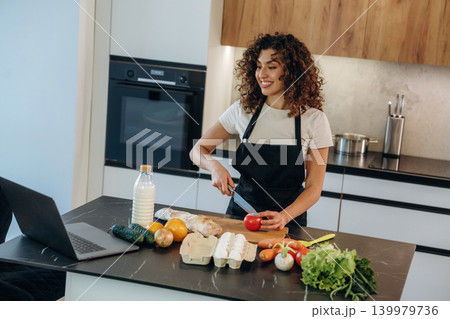 Slicing the tomato. Attractive woman preparing fresh vegetables on the kitchen counter during cooking Slicing the tomato. Attractive woman preparing fresh vegetables on the kitchen counter during cooking 139979736