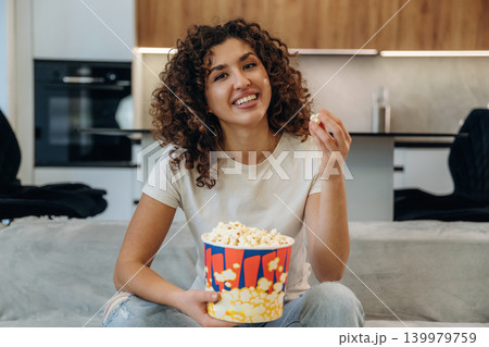 Tasty meal. Happy woman relaxing on a sofa with popcorn, watching TV and enjoying her leisure time at home 139979759