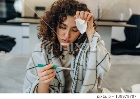 Checking temperature. Sick woman feeling unwell at home and using medicine while resting on a sofa 139979787