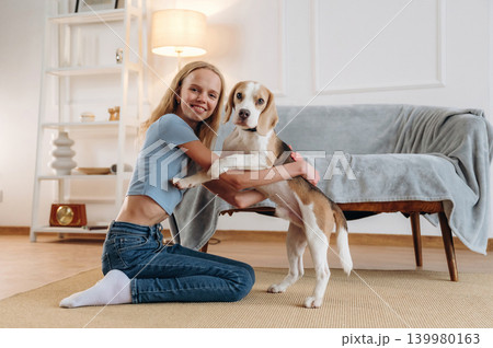 Smiling, having fun. Girl is with her dog on the floor in a cozy living room Smiling, having fun. Girl is with her dog on the floor in a cozy living room 139980163