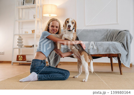 Smiling, having fun. Girl is with her dog on the floor in a cozy living room 139980164