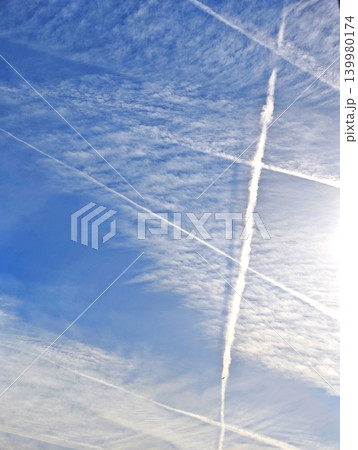 Multiple intersecting white condensation trails from airplanes crossing in a bright blue sky, creating abstract geometric patterns against the vast atmosphere 139980174