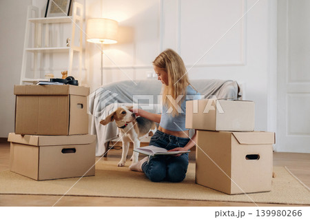 Bunch of boxes, new home, relocation. Girl is with her dog on the floor in a cozy living room Bunch of boxes, new home, relocation. Girl is with her dog on the floor in a cozy living room 139980266