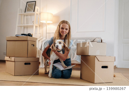 Bunch of boxes, new home, relocation. Girl is with her dog on the floor in a cozy living room 139980267