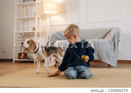 Yellow toy car holding in hand. Cute little boy playing with dog at home on the floor Yellow toy car holding in hand. Cute little boy playing with dog at home on the floor 139980279