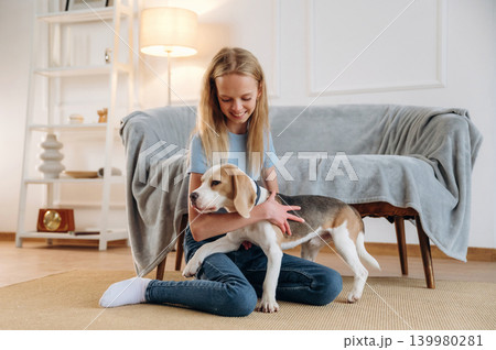 Smiling, having fun. Girl is with her dog on the floor in a cozy living room 139980281