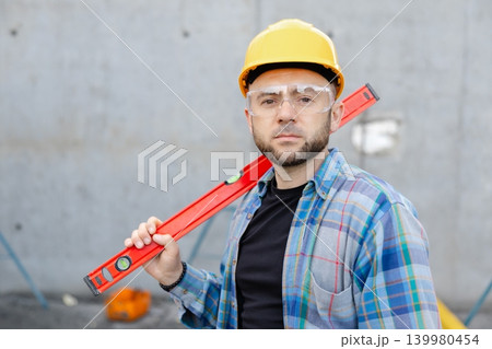 Construction worker wearing hard hat and safety glasses holding spirit level Construction worker wearing hard hat and safety glasses holding spirit level 139980454