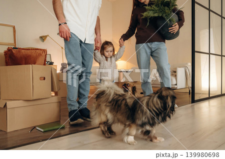 Particle view, holding kid by hands. Happy young family with child and dog moving into new home, standing among cardboard boxes Particle view, holding kid by hands. Happy young family with child and dog moving into new home, standing among cardboard boxes 139980698