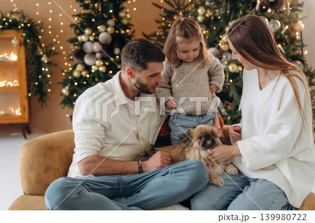 Pet is on the legs. Happy family with child and dog celebrating Christmas together at home with decorated tree Pet is on the legs. Happy family with child and dog celebrating Christmas together at home with decorated tree 139980722