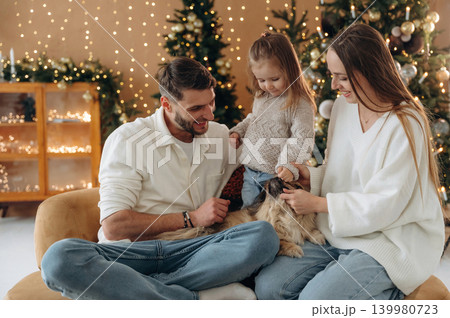 Pet is on the legs. Happy family with child and dog celebrating Christmas together at home with decorated tree 139980723