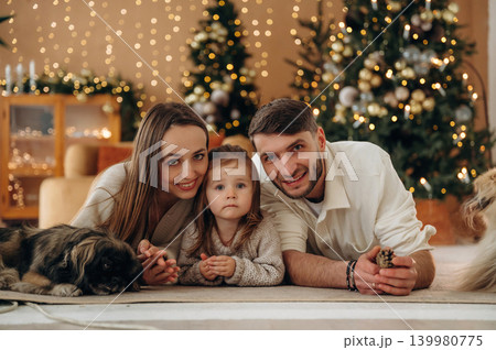 Front view, lying down. Happy family with child and dog celebrating Christmas together at home with decorated tree Front view, lying down. Happy family with child and dog celebrating Christmas together at home with decorated tree 139980775