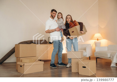 Cheerful young family with child moving into new home, standing among cardboard boxes 139980777