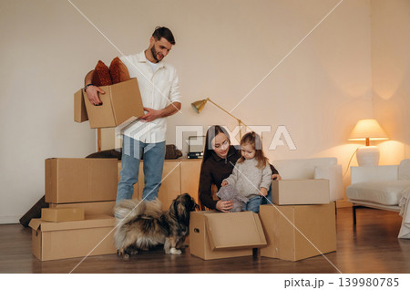 Conception of new life. Happy young family with child and dog moving into new home, standing among cardboard boxes Conception of new life. Happy young family with child and dog moving into new home, standing among cardboard boxes 139980785
