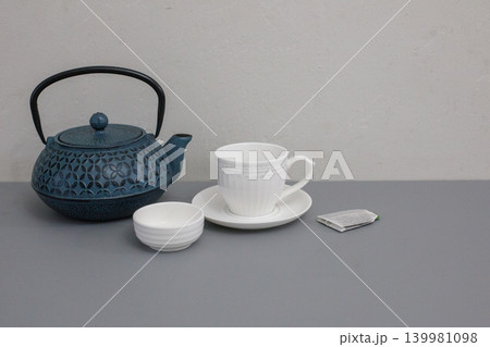 A teapot sits next to a cup on a plate. 139981098