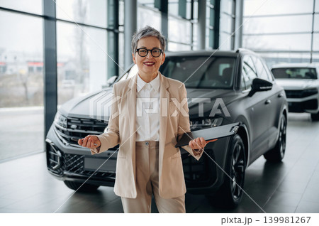 Confident businesswoman in stylish suit stands in modern car showroom, showcasing luxury vehicles and demonstrating professionalism in automotive sales Confident businesswoman in stylish suit stands in modern car showroom, showcasing luxury vehicles and demonstrating professionalism in automotive sales 139981267