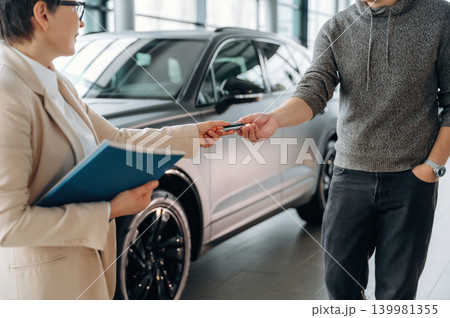 Customer receiving car keys from sales representative in modern showroom, showcasing vehicle purchase process and customer service experience Customer receiving car keys from sales representative in modern showroom, showcasing vehicle purchase process and customer service experience 139981355