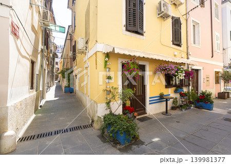 A narrow street is lined with colorful buildings, with potted plants and flowers adorning the entrances in Piran, Slovenia A narrow street is lined with colorful buildings, with potted plants and flowers adorning the entrances in Piran, Slovenia 139981377